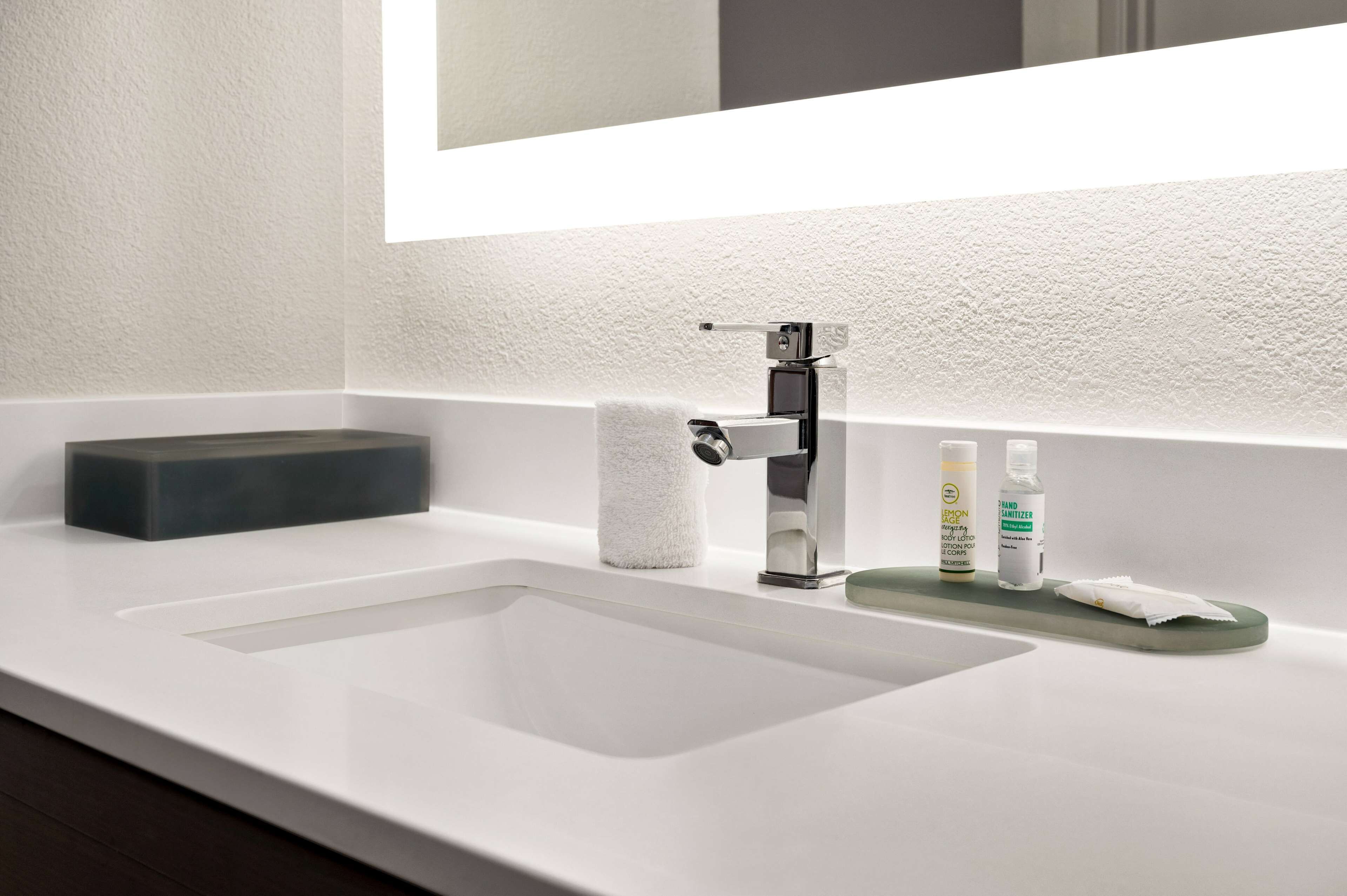 A modern bathroom with a white sink, a mirror, and a soap dispenser.