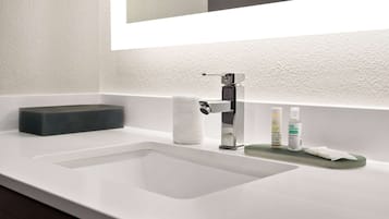 Un baño moderno con un lavabo blanco, un espejo y un dispensador de jabón.