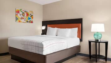 A hotel room with a bed, a nightstand, a lamp, and a wall art piece.