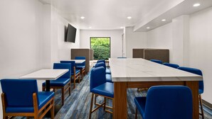 Een vergaderzaal met een lange tafel, blauwe stoelen en een televisie aan de muur.