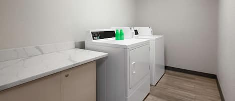 A laundry room with two white washing machines, a control panel, and two green bottles on the counter.