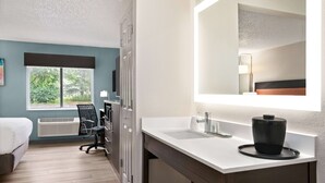 Een moderne hotelkamer met een bed, bureau, stoel en een groot raam.