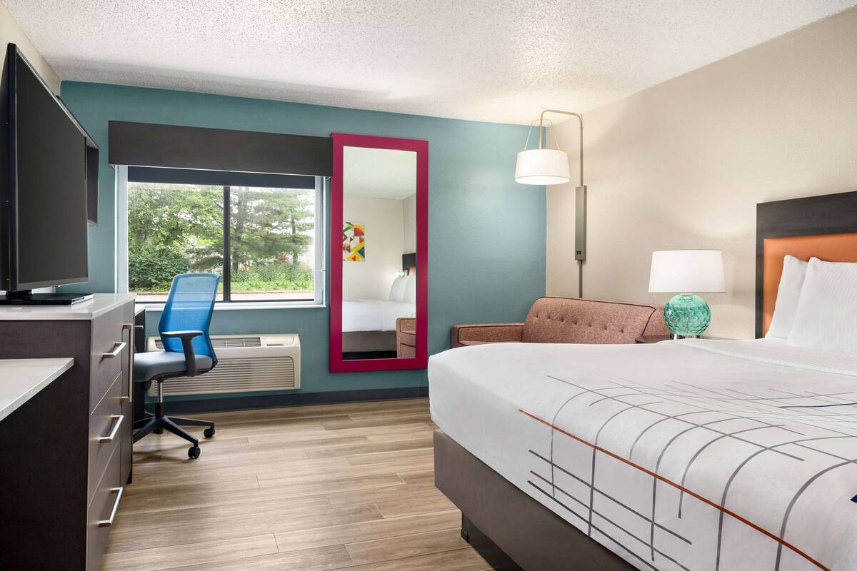 A hotel room with a bed, desk, chair, and a large window.