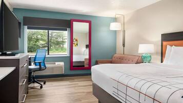 A hotel room with a bed, desk, chair, and a large window.