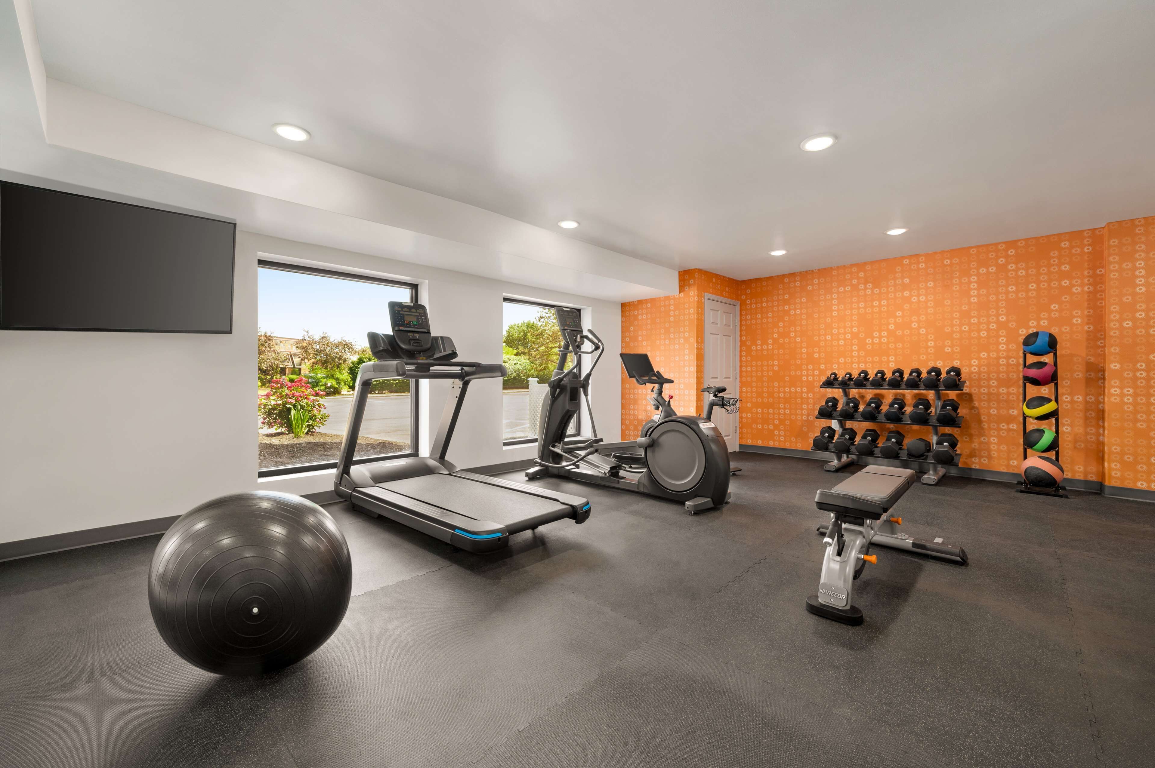 Un gimnasio moderno con cintas de correr, una elíptica, un banco de pesas y varias pesas.