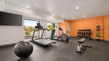 Un gimnasio moderno con cintas de correr, una elíptica, un banco de pesas y varias pesas.