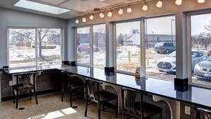A restaurant with a long counter, several chairs, and large windows offering a view of a parking lot and buildings outside. - Quality Inn & Suites North/Polaris (Columbus)