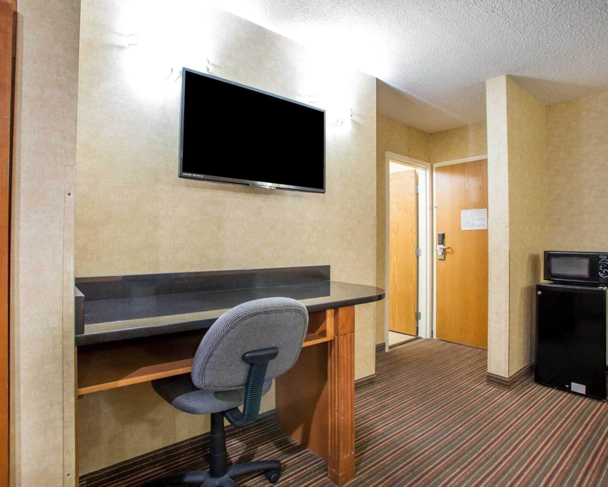 Een hotelkamer met een flatscreen televisie aan de muur, een bureau met stoel en een magnetron op een bijzettafeltje.