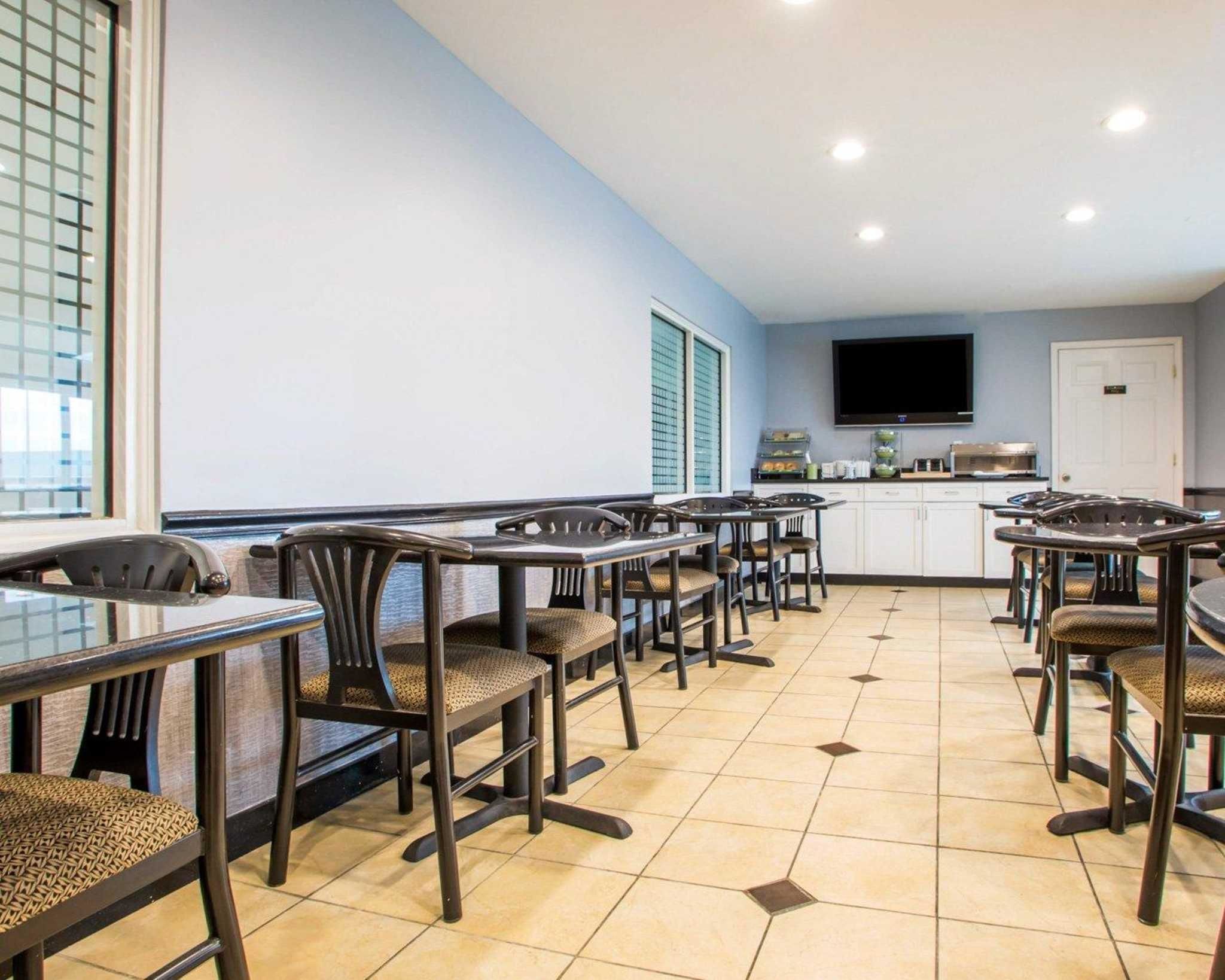 A dining area with multiple tables and chairs, a kitchen area with a flat-screen TV, and a window with blinds.