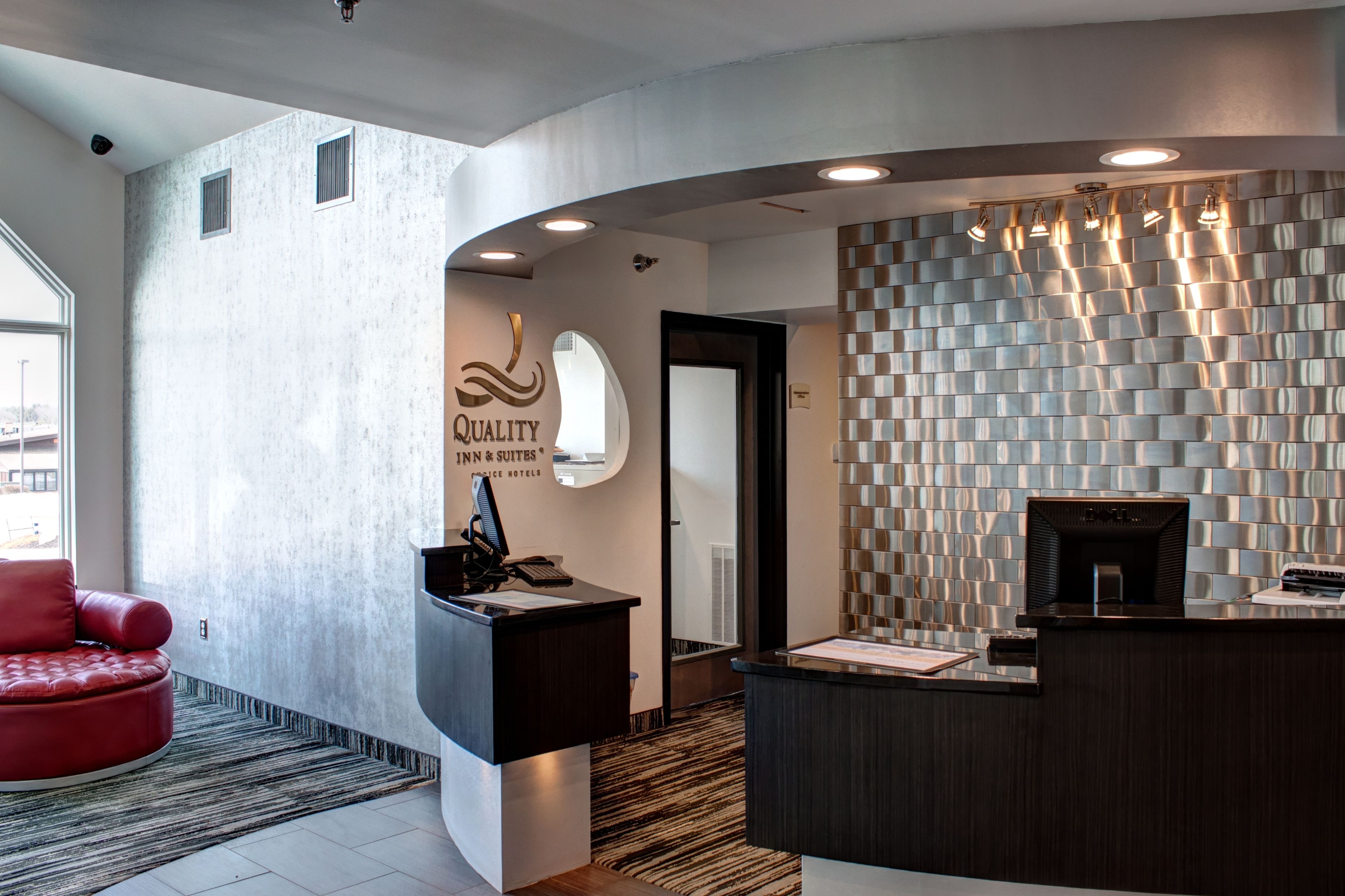 A hotel reception area with a modern design, including a reception desk, a red leather chair, and a wall with a textured pattern.