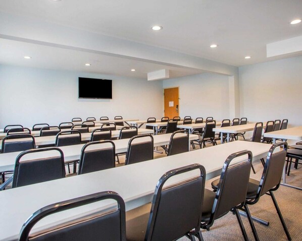 A conference room with long tables and chairs, a flat-screen TV, and a door.