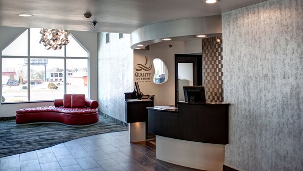 A reception area with a modern design, featuring a red sofa, a reception desk, and a large window offering a view of the outside. - Quality Inn & Suites North/Polaris (Columbus)