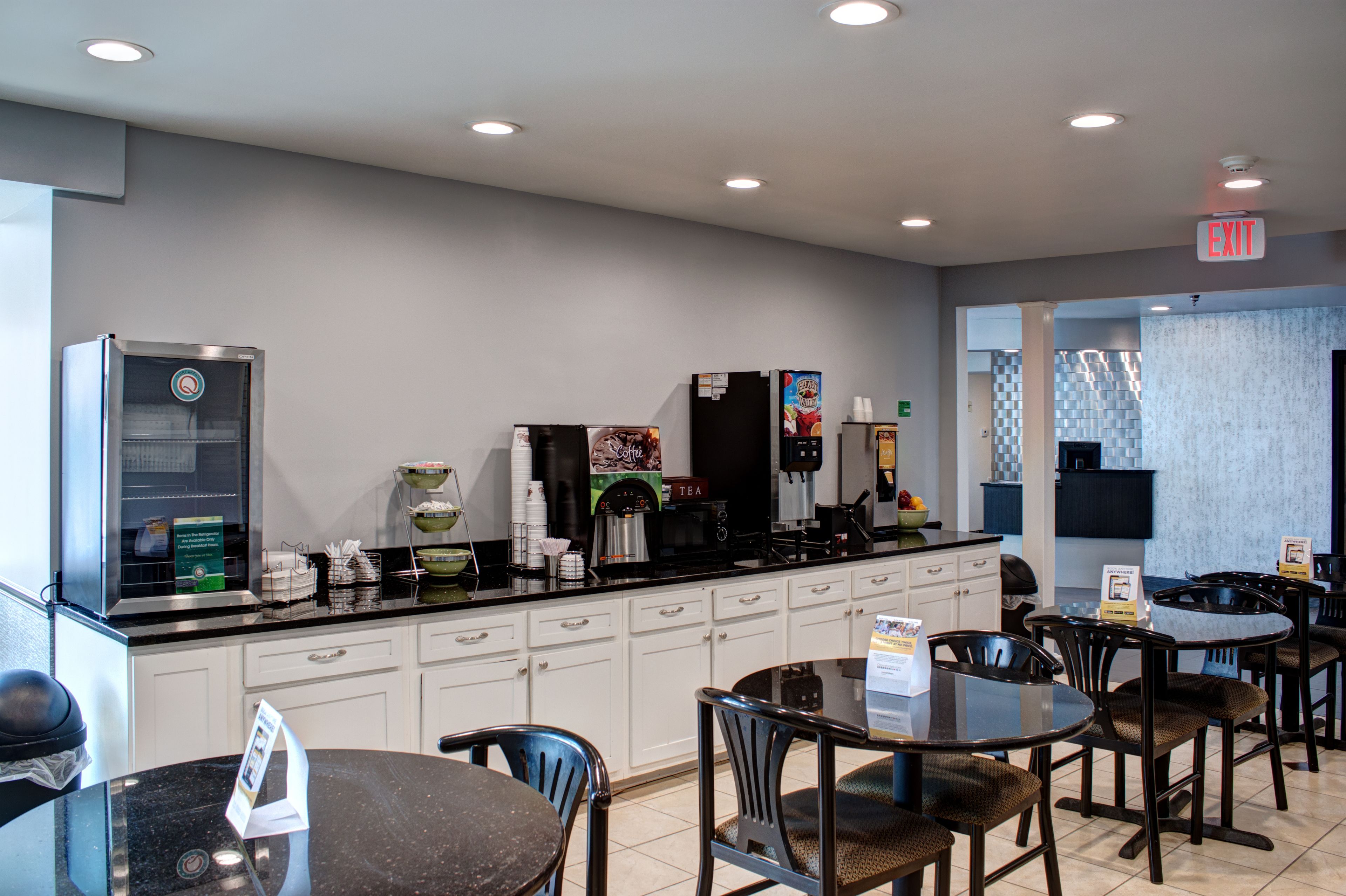 Un moderno caffè con un angolo self-service per il caffè, zona con posti a sedere e cartello di uscita.
