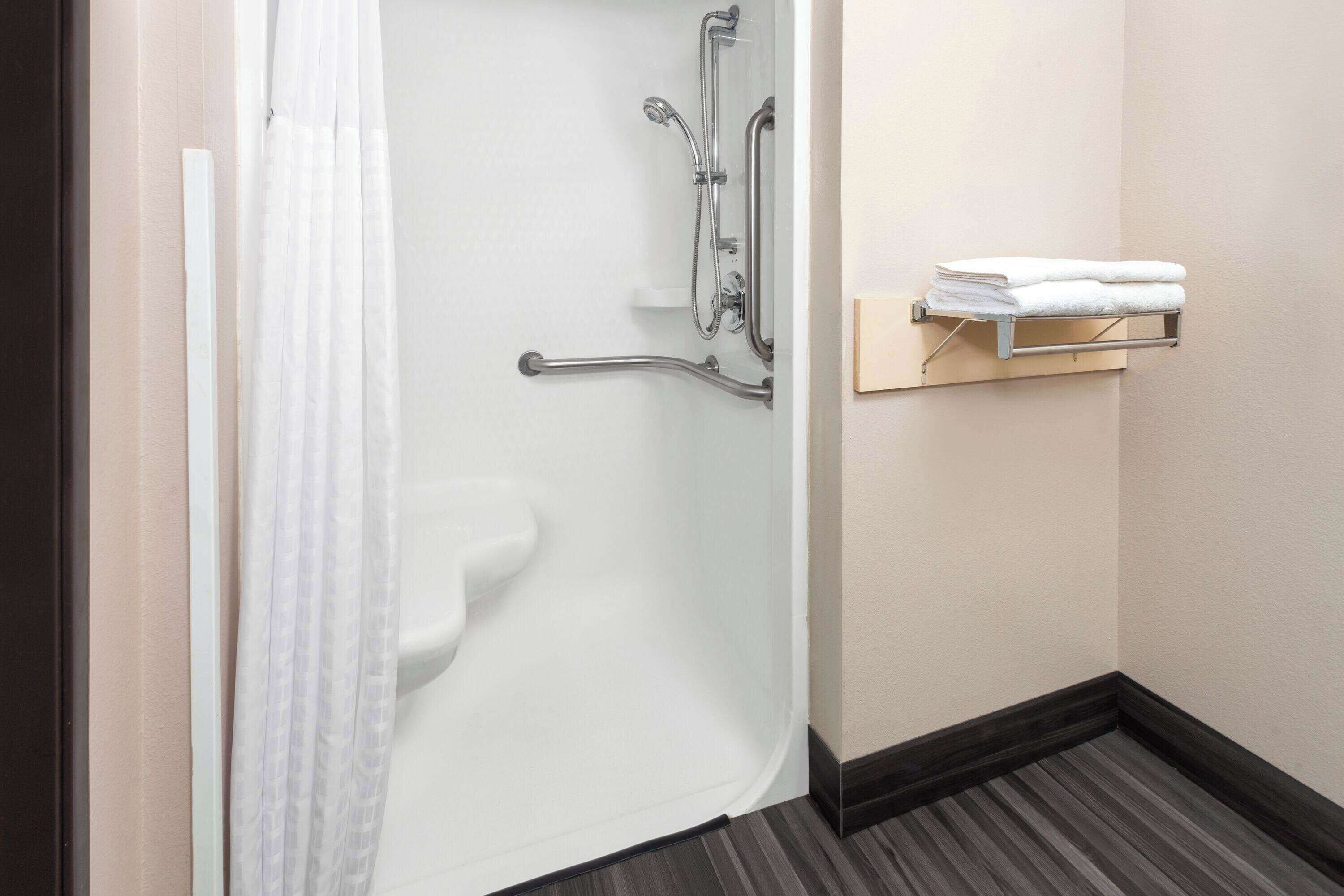 A bathroom with a shower, grab bars, a towel rack, and a toilet.