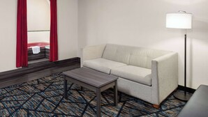 Habitación de hotel con sofá, una mesita, lámpara de pie y alfombra estampada.