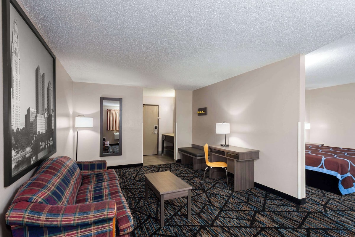 Hotelkamer met een bank, bureau, stoel, bed, lamp en een lijst met een stadsgezicht.