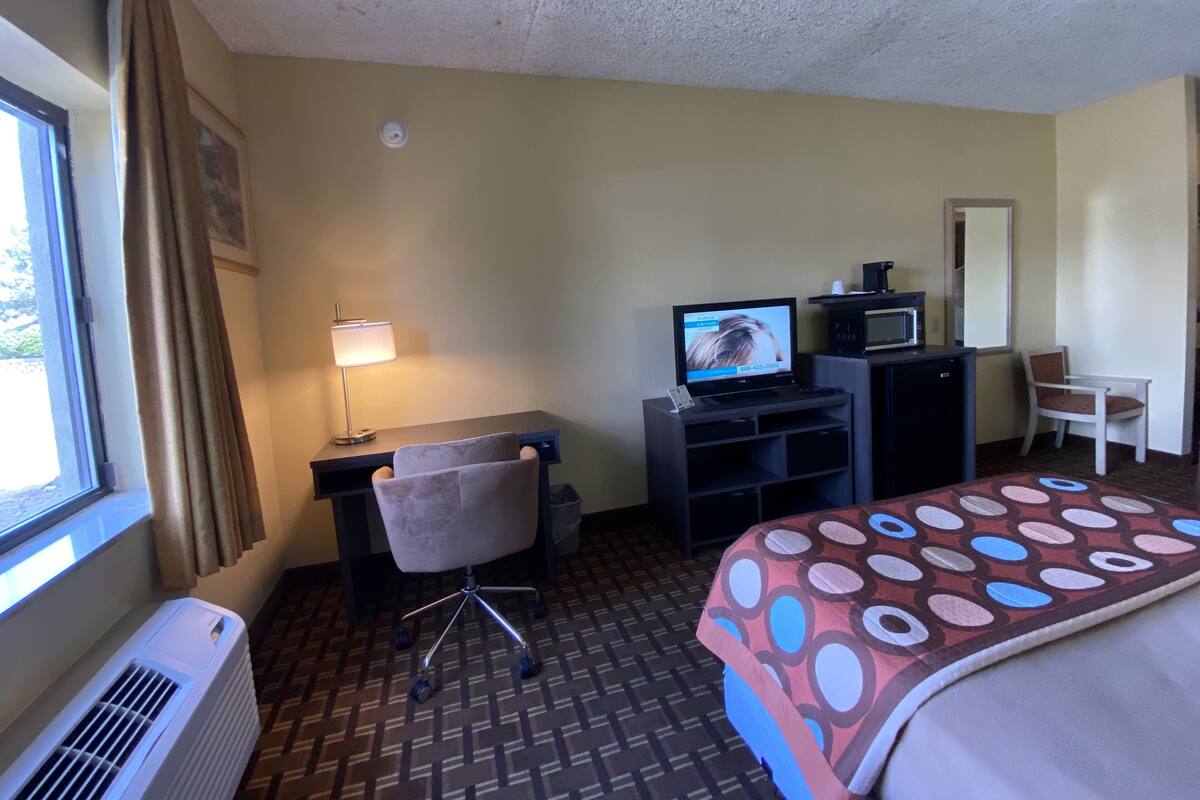 A hotel room with a bed, desk, chair, television, air conditioner, and a window with curtains.