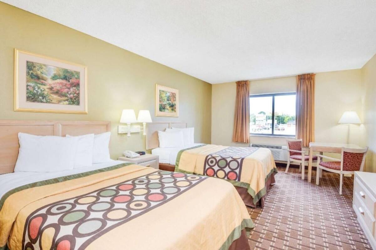 A hotel room with two beds, a desk, chairs, and a window with curtains.