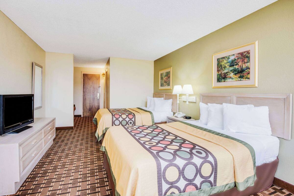 A hotel room with two beds, a TV, a desk, and a painting on the wall.