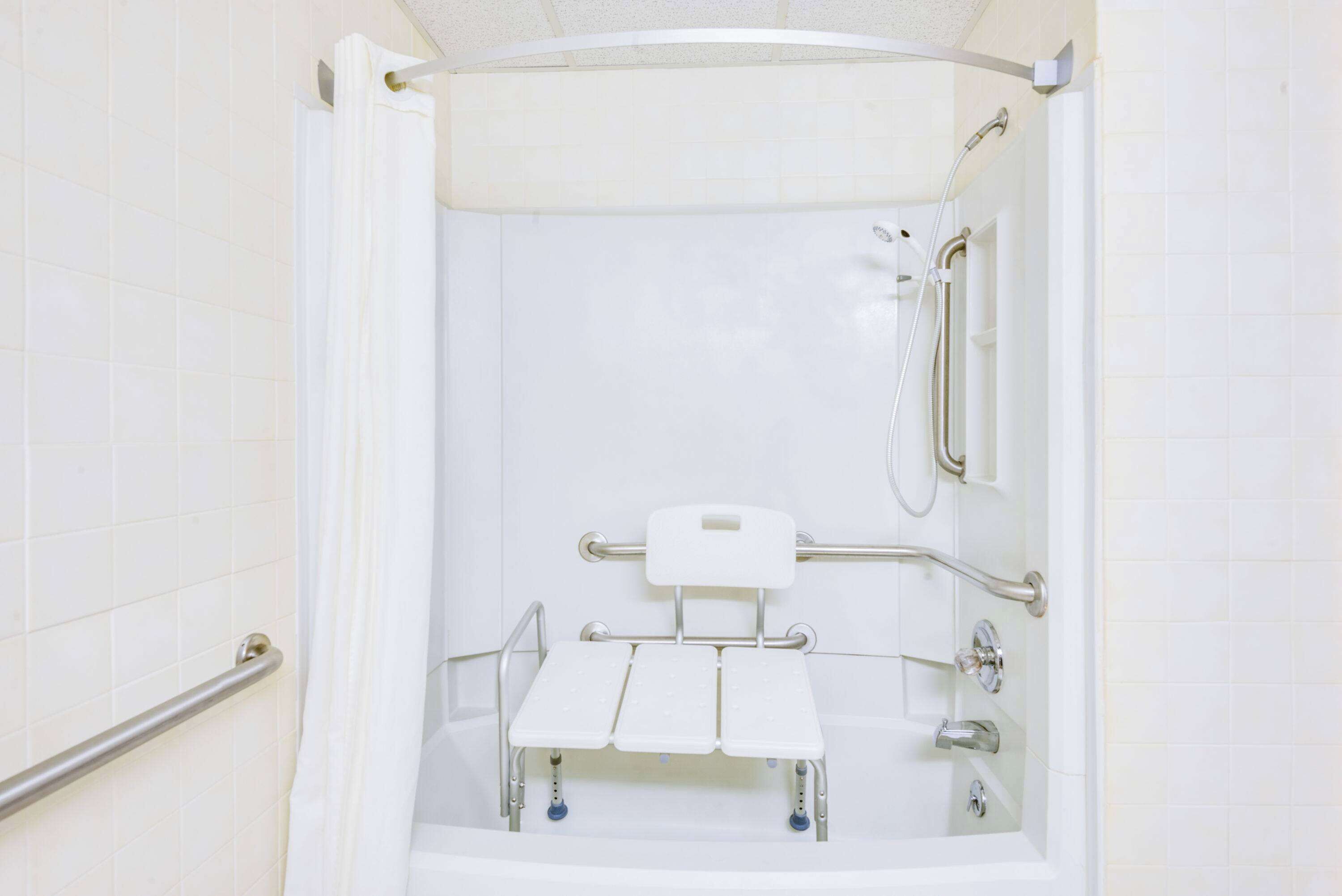 Un baño con una bañera blanca, barras de apoyo, un cabezal de ducha y un accesorio de ducha manual.