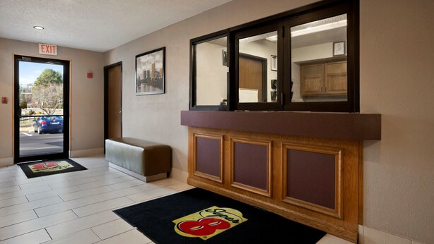 A hotel lobby with a reception desk, a bench, an exit sign, and a door leading outside. - Super 8 by Wyndham Richmond/Chamberlayne Rd (Richmond)