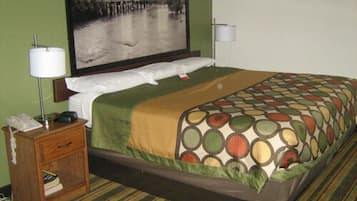 Quarto de hotel com cama, mesa de cabeceira, abajur, telefone e um quadro na parede.