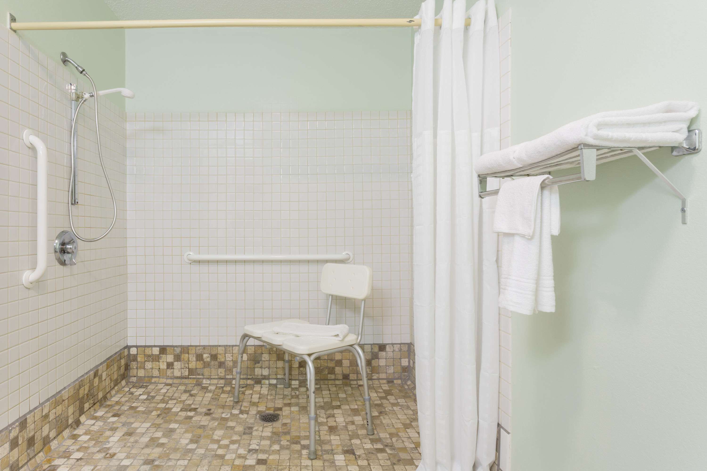 Zona de ducha accesible en silla de ruedas, con barra de apoyo, ducha y asiento.