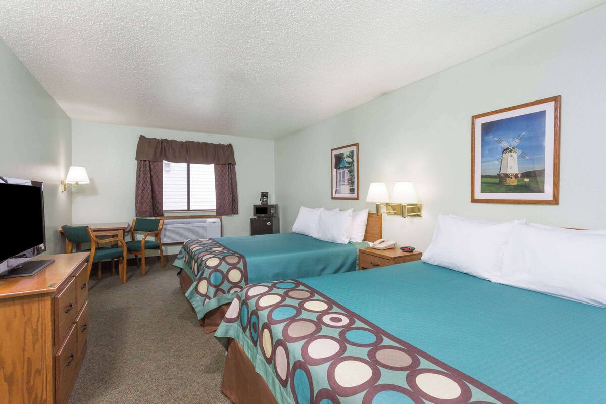 A hotel room with two beds, a desk with a chair, a TV, and a window with curtains.