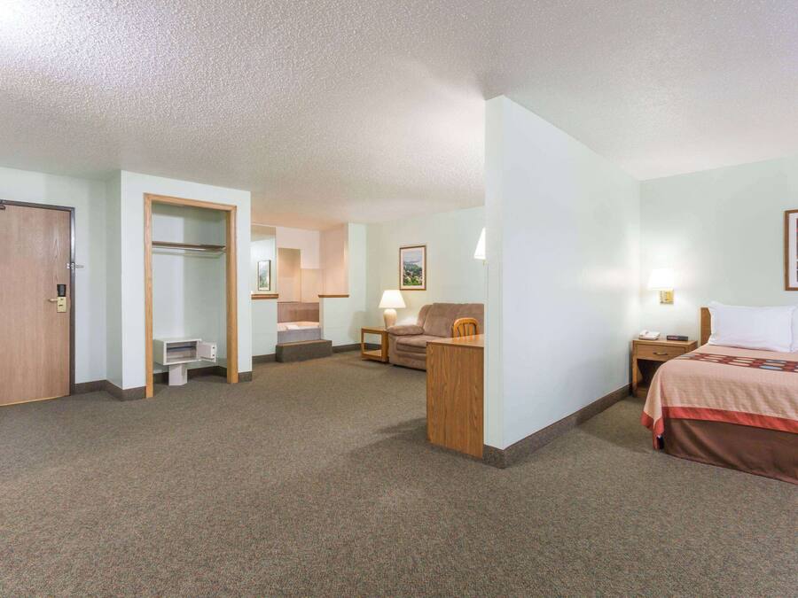 A hotel room with a bed, a desk, a chair, a couch, a door, and a small bathroom.