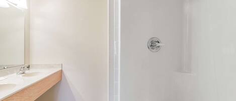 Un baño con lavamanos blanco, espejo y ducha.