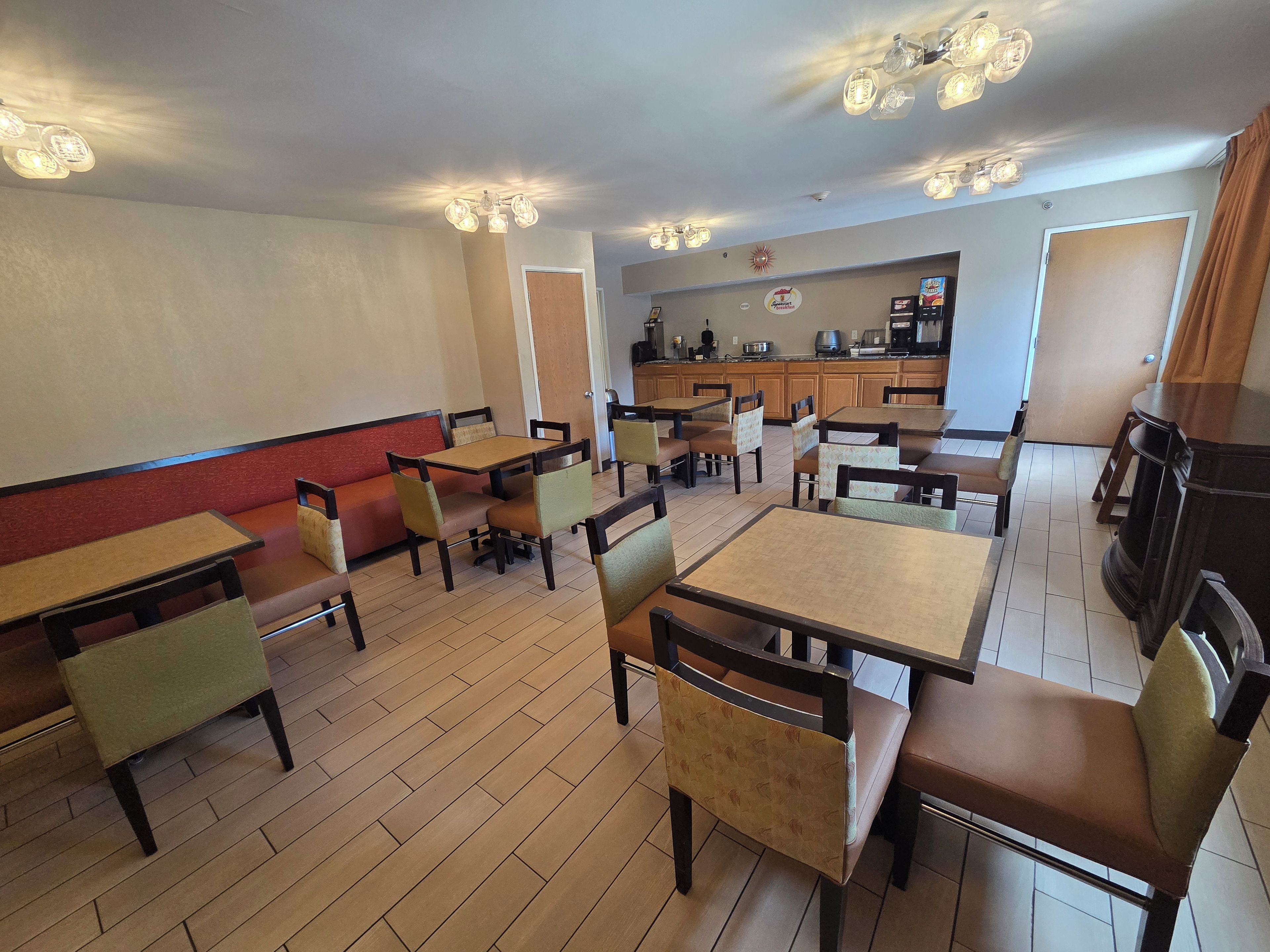 A restaurant interior with multiple tables and chairs, a kitchen area in the background, and a ceiling with hanging lights.