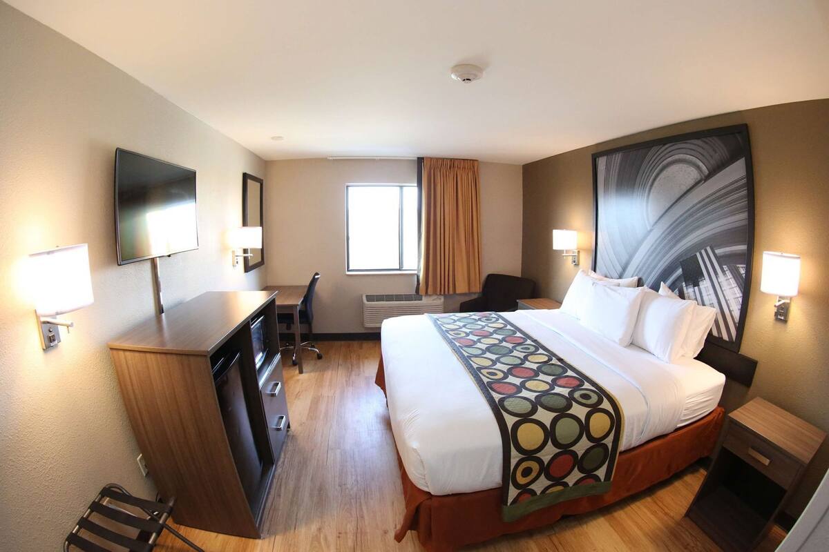 Habitación de hotel con cama, escritorio, silla, televisor y obras de arte en las paredes.