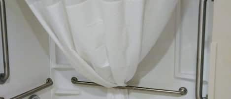 A bathroom with a white bathtub, grab bars, and a white shower curtain.