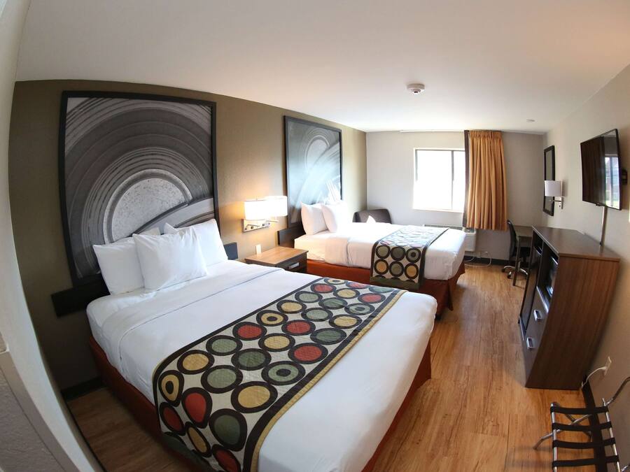 A hotel room with two beds, a desk, a chair, a TV, and a large abstract painting on the wall.