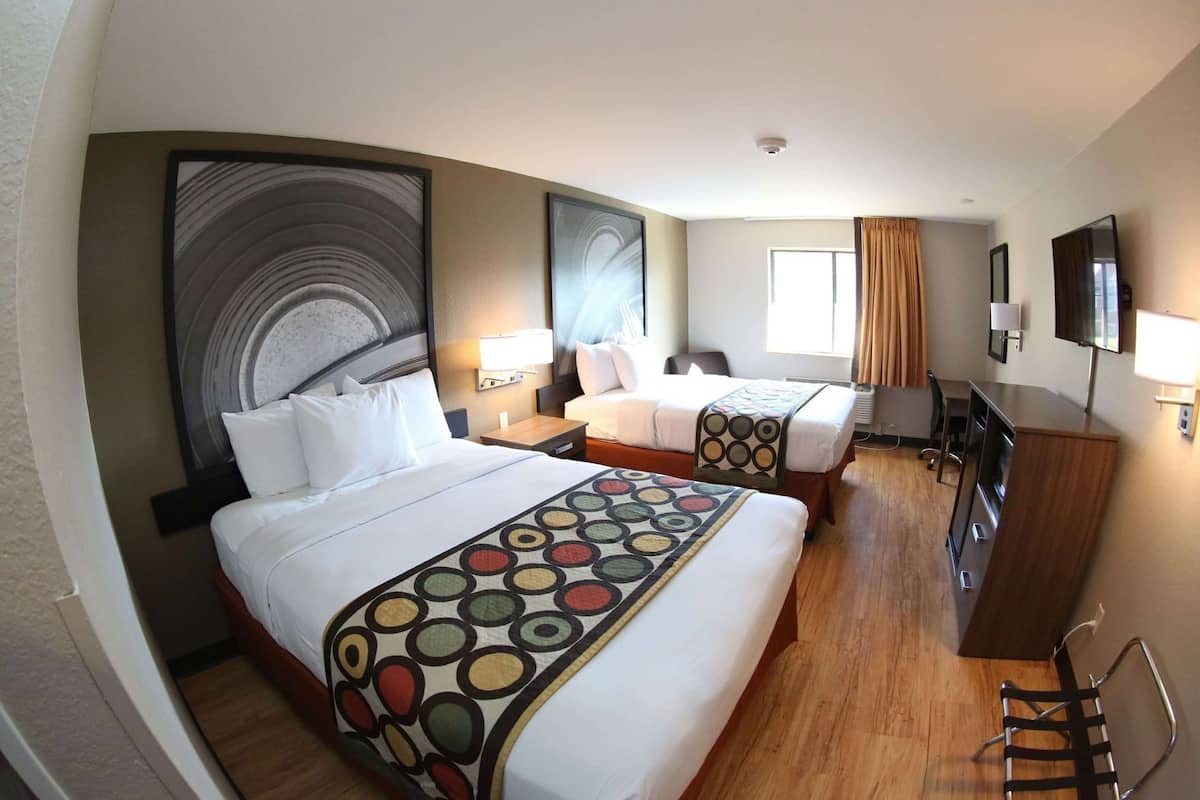 Habitación de hotel con dos camas, un escritorio, una silla, un televisor y obras de arte en las paredes.