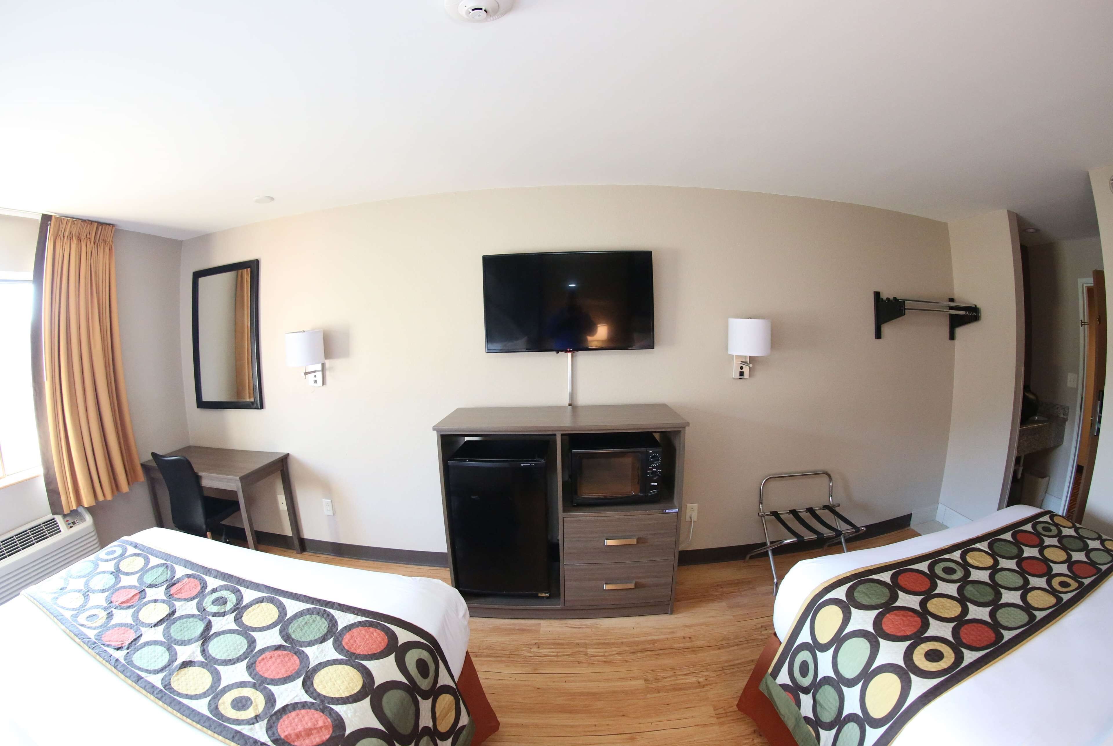 A hotel room with two beds, a desk, a flat-screen TV, a microwave, and a small seating area.