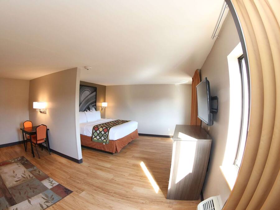A hotel room with a bed, a desk with a chair, a TV mounted on the wall, and a large window with curtains.