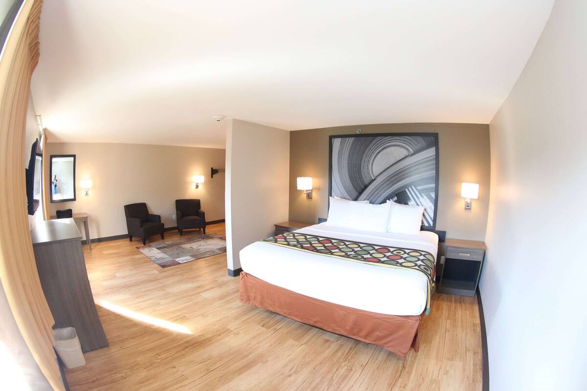 Una habitación de hotel con una cama grande, dos mesitas de noche, un escritorio, una silla y un televisor instalado en la pared.