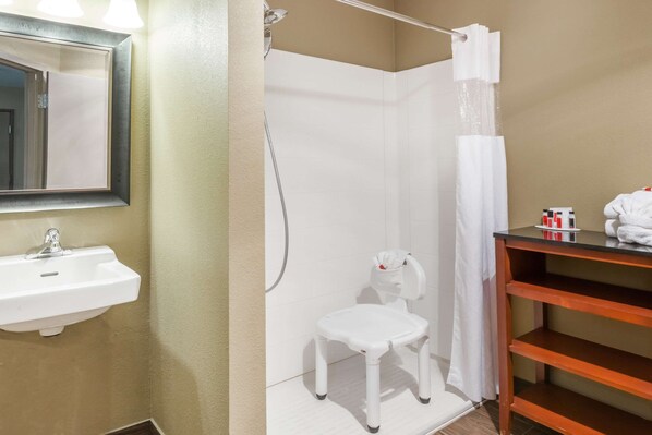 A bathroom with a white sink, a shower, a white chair, and a wooden shelf with toiletries.