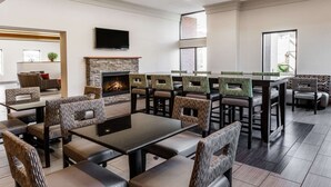 A modern indoor dining area with a stone fireplace, comfortable seating, and a flat-screen TV mounted on the wall. - Wingate by Wyndham Canton/Hall of Fame (Canton)