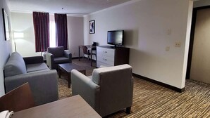 A hotel room with a sofa, armchairs, a small table, a TV, a desk, and a chair. - Wingate by Wyndham Canton/Hall of Fame (Canton)