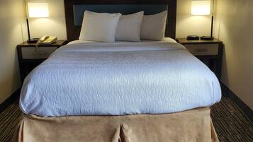 Una habitación de hotel con una cama grande, dos mesitas de noche, una lámpara y un teléfono.