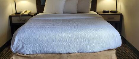 A hotel room with a large bed, two bedside tables, a nightstand, a lamp, and a telephone.