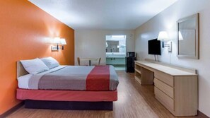 A hotel room with a bed, a desk, a chair, a TV, and a mirror.