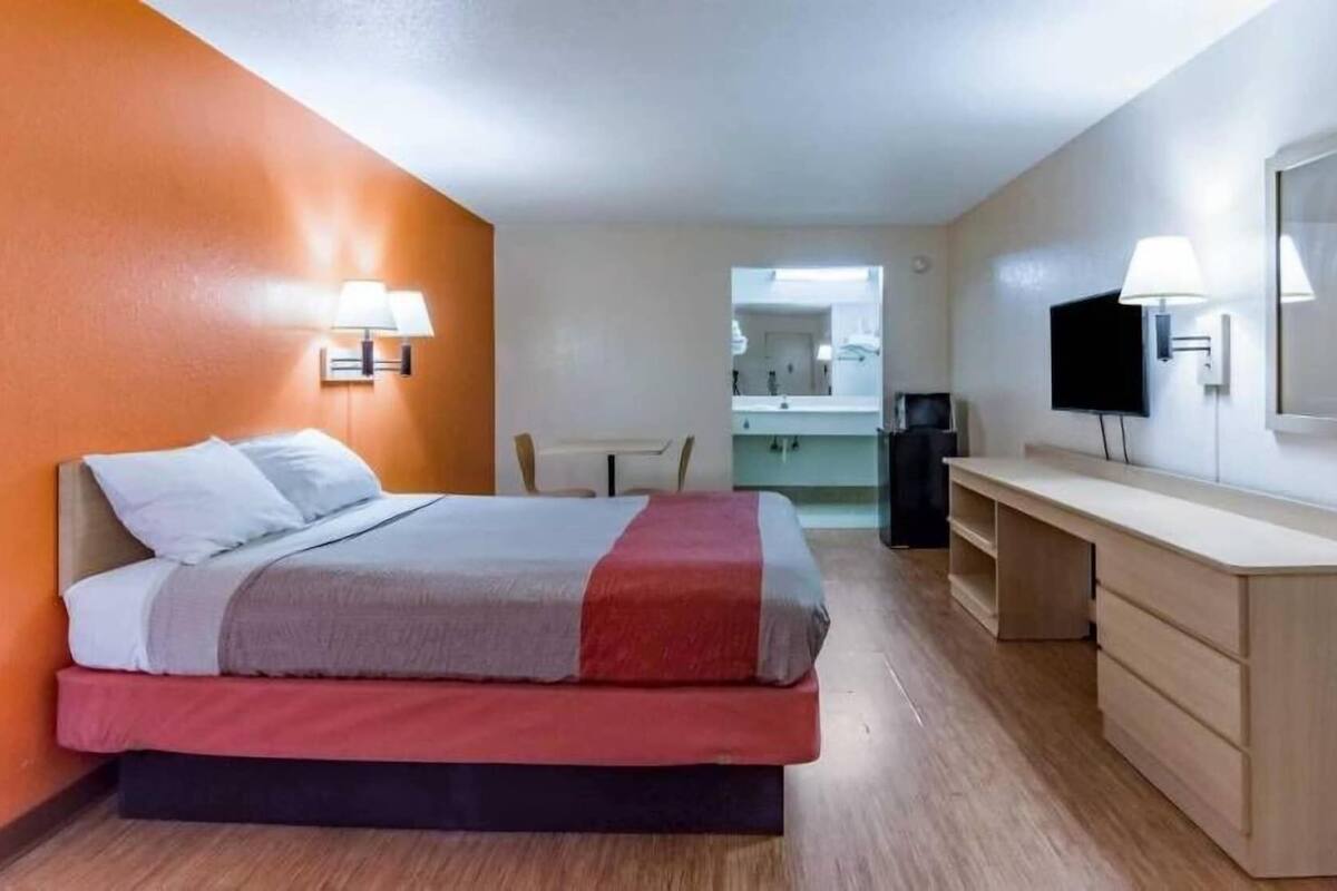 A hotel room with a bed, a desk, a chair, a TV, and a mirror.