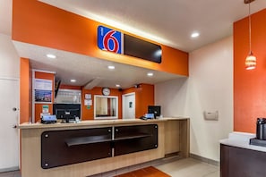 A reception desk with a digital clock, a sign indicating room availability, and a counter with a coffee machine.