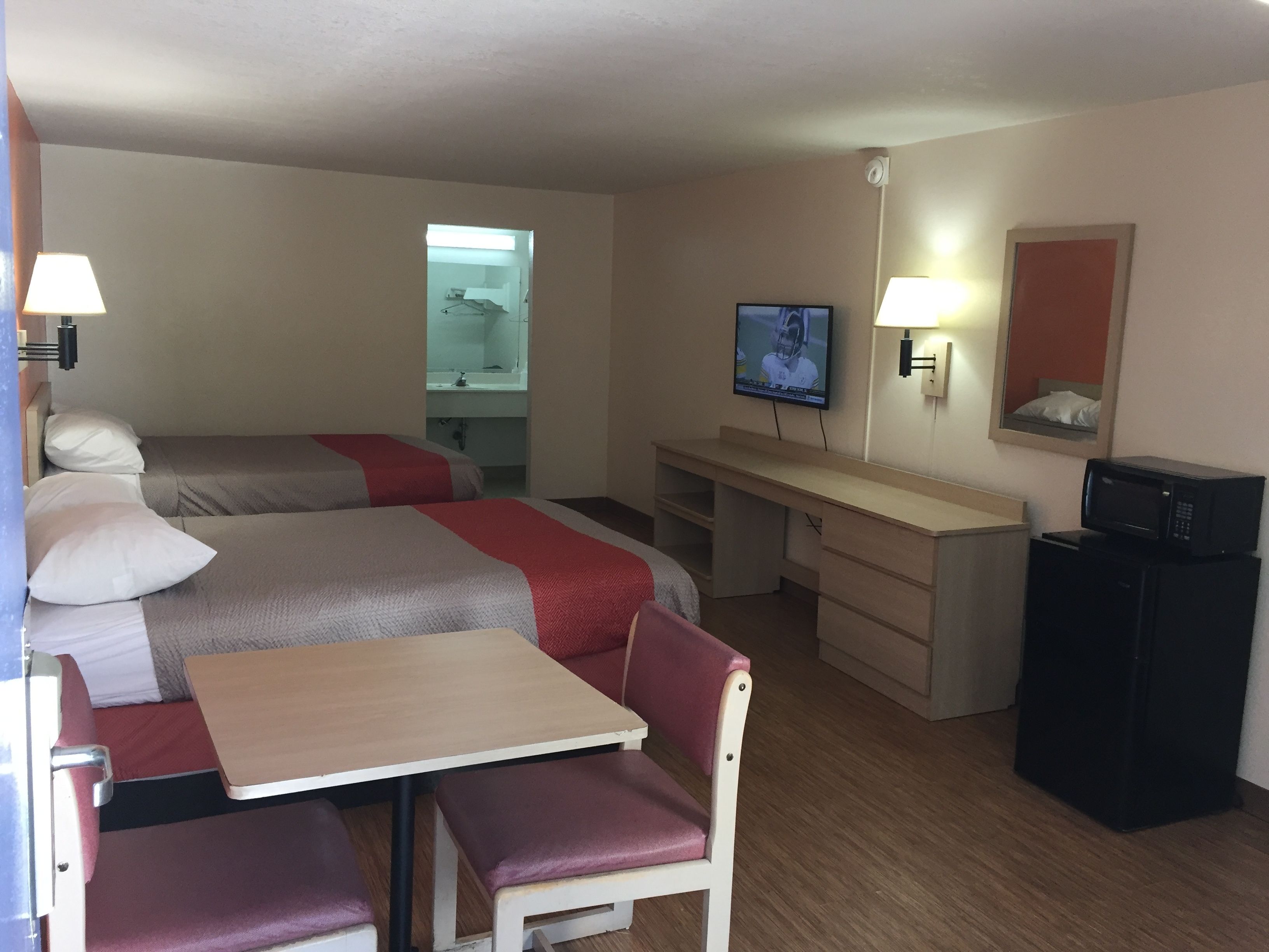 Une chambre d’hôtel avec deux lits, un bureau, une chaise, une télévision, un miroir et un four à micro-ondes.