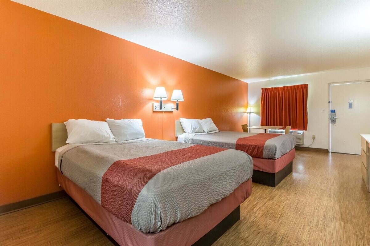 A hotel room with two beds, a desk, a chair, and a window with curtains.
