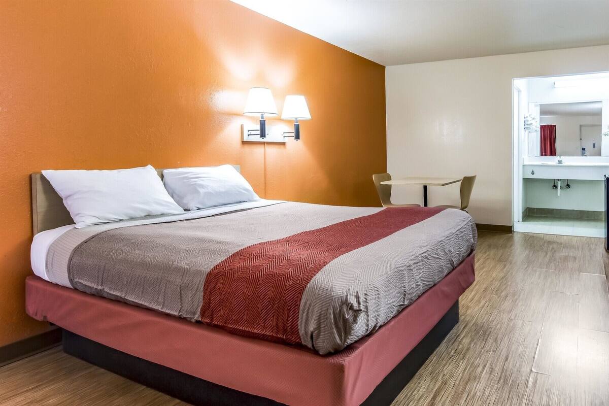 A hotel room with a bed, two wall-mounted lamps, a small table, and a chair.