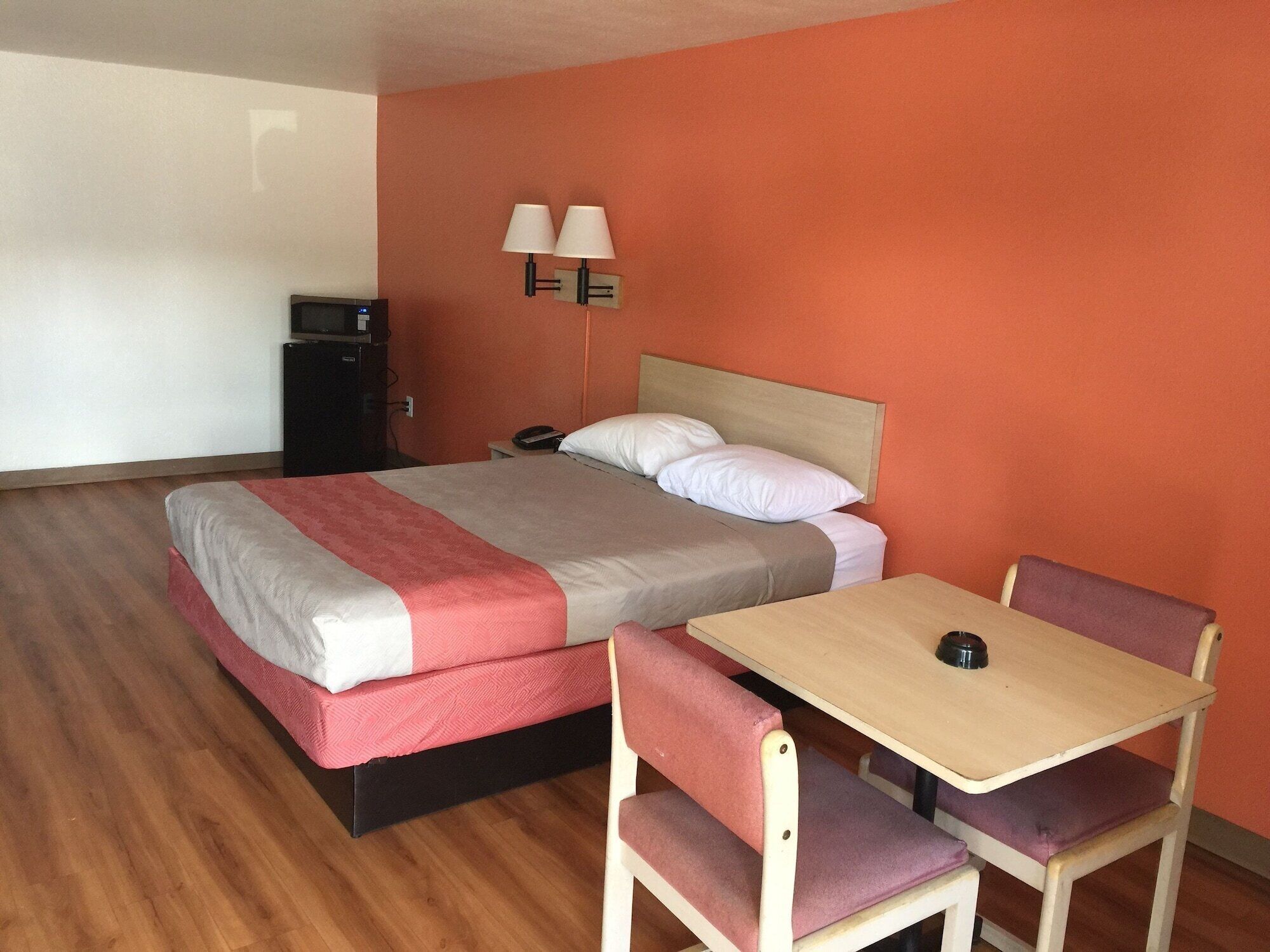 A hotel room with a bed, bedside table, chairs, a desk, a lamp, and a TV.